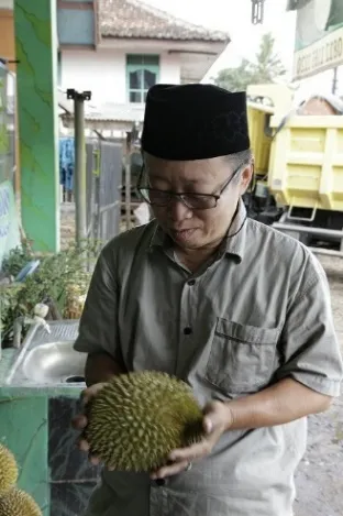 Pria berkopiah hitam memegang durian di depan warung