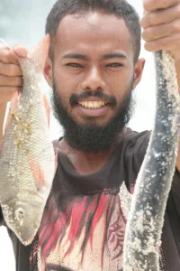 Pemuda berjanggut memegang dua ekor ikan hasil pancingan