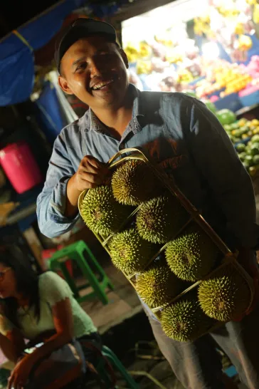 Pedagang tersenyum menenteng durian dalam wadah bambu