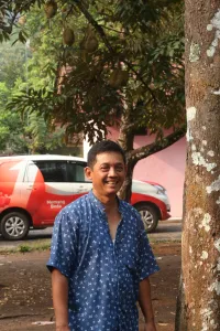 Pria berkemeja batik biru berdiri di bawah pohon durian
