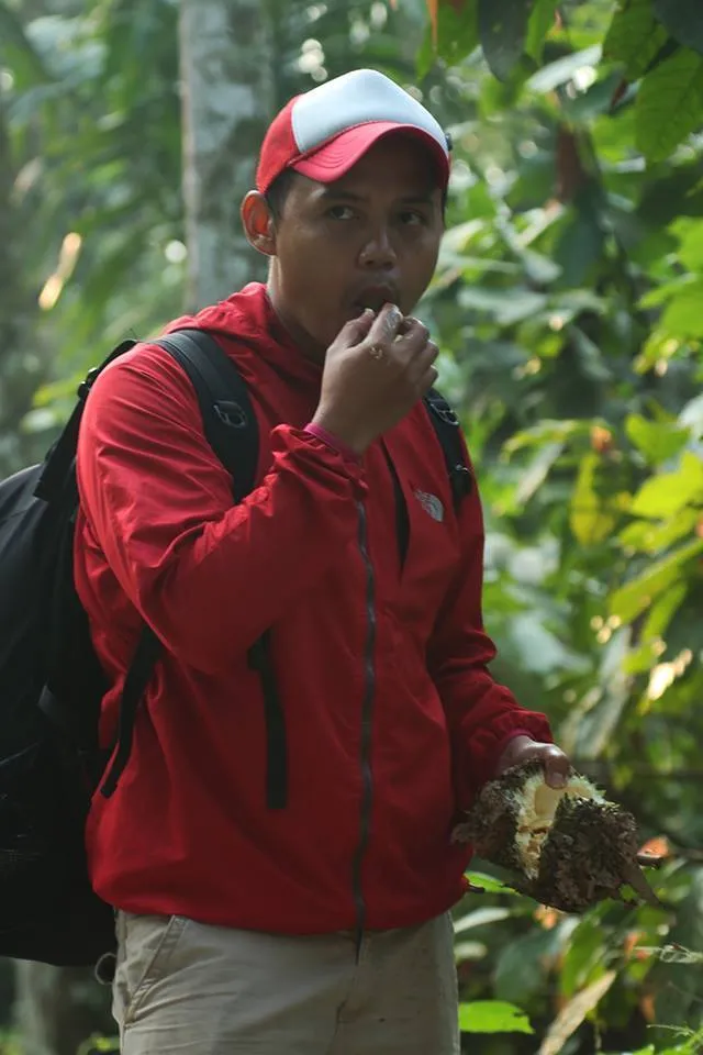 Pria bertopi merah mencicipi durian di tengah parak