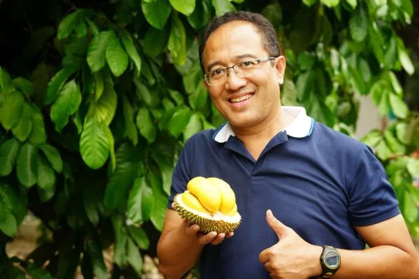Pria berkacamata tersenyum memegang durian Empe berdaging kuning