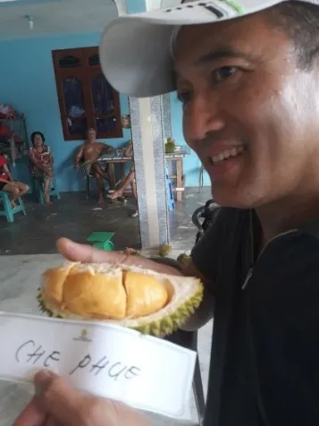 Pria bertopi memegang durian Che Puy berdaging kuning dan kartu namanya