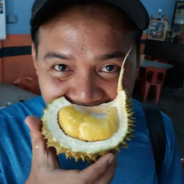 Pria bertopi berpose dengan sebelah durian berdaging kuning di depan mulut