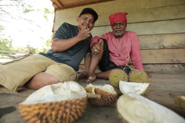 Dua pria duduk di depan durian-durian yang telah dibuka